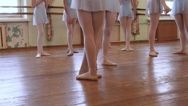 Legs of ballerinas in blue suits standing on floor and walk away during ballet class.