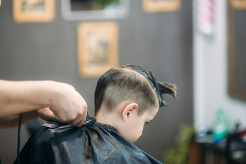 Little boy on a haircut in the barber sits on a chair.