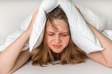 Woman with insomnia covering head and ears with pillow - obrazy, fototapety, plakaty