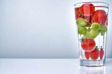 Cherry tomatos and grapes in a cocktail glas in water with copy space. Concept for healthy eating.