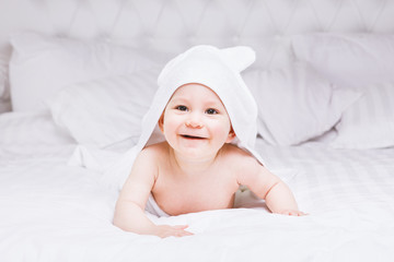 Fototapeta na wymiar Adorably baby lie on white towel in bed. Happy childhood and healthcare concept.