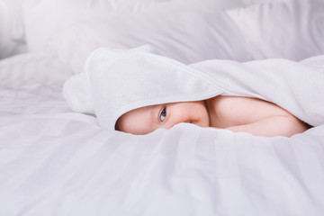 Adorably baby lie on white towel in bed. Happy childhood and healthcare concept.