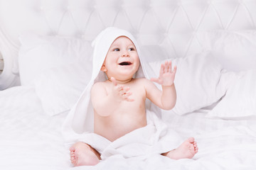 Fototapeta na wymiar Adorably baby lie on white towel in bed. Happy childhood and healthcare concept.