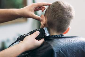 Little Boy Getting Haircut By Barber While Sitting In Chair At Barbershop.