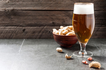 glass of light cold frothy beer, nuts on an old wooden background