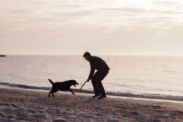 young man having fun with dog on the morning beach