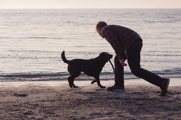 young man having fun with dog on the morning beach