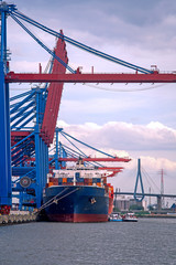 Large container ship being unloaded by container cranes in dock near Hamburg