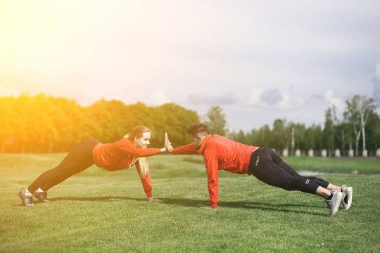 Sport And Fitness Man And Woman Training In Green Park Face To Face All Together. Couple Doing Athletic Exercises Outdoors. Toned.