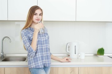 Beautiful young woman holds a glass with water on kitchen.