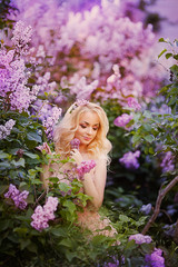 Beautiful woman enjoying lilac garden, young woman with flowers in green park. cheerful teenager walking outdoor. soft light style color.Young girl in beautiful wreath of lilac flowers