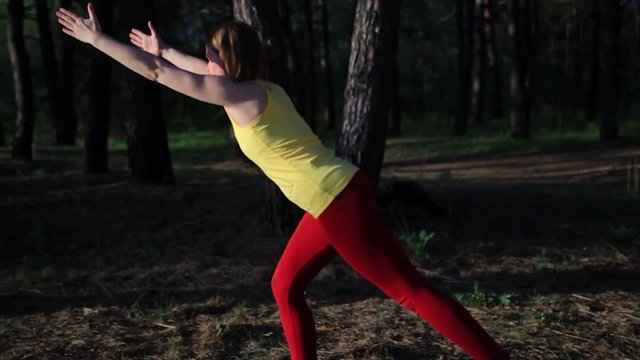 Girl practicing yoga stretching at sunset in forest. Slow motion shot.