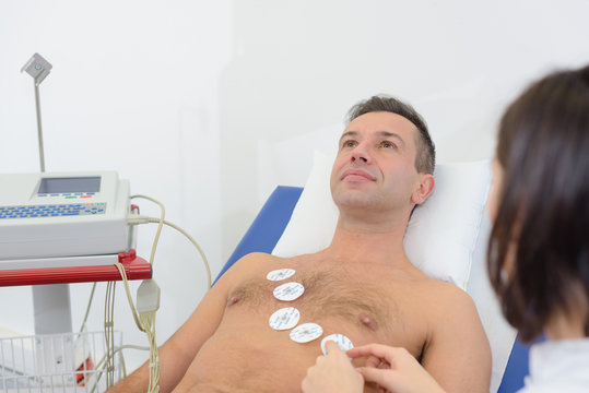 Nurse attaching pads to man's chest for heart monitoring