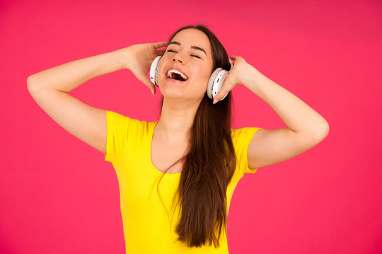 Beautiful young woman in black and yellow vibrant dress dances as she listens to the music over pink background