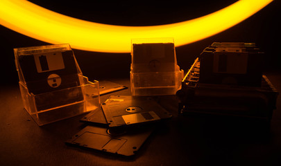 Fototapeta na wymiar Pile of black floppy disks on dark background with light. Vintage computer attributes