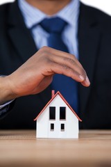 Businessman protecting house model with hands