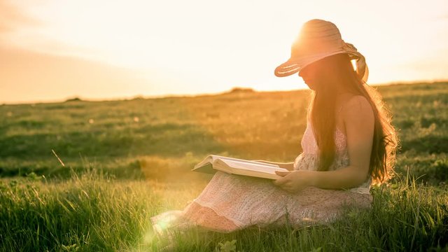 Girl reading the book on rural landscape against sunset