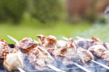 Grilled kebab cooking on metal skewer closeup. Roasted meat cooked at barbecue. Traditional eastern dish, shish kebab. Grill on charcoal and flame