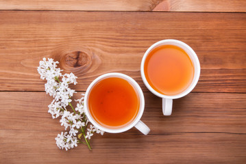 Two cups of tea and a lilac bud on a wooden background.
