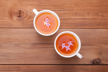 Two cups of tea with lilac flowers on a wooden background.
