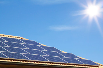 Photovoltaic panels on the roof of a residential building for alternative energy production in front of blue sky with sunshine and copyspace
