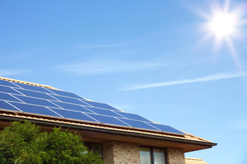 Photovoltaic panels on the roof of a residential building for alternative energy production in front of blue sky with sunshine and copyspace
