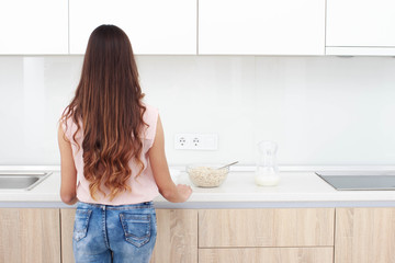 Back view of little girl with long curly hair standing at a kitchen