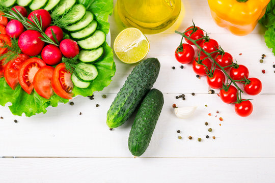 Cucumbers, radish, tomatoes cherry, olive oil, herb and spices on old white wooden background. Set for healthy foods. Ingredients for salad.