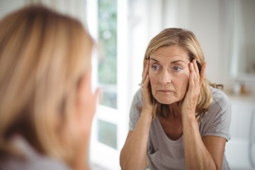 Frustrated senior woman looking at mirror