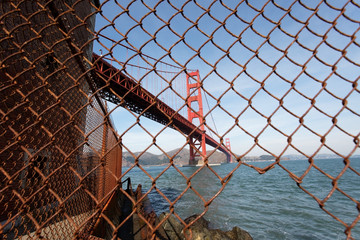Unusual view of the Golden Gate Bridge seen through rusty chain link fence.