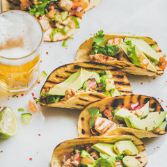 Healthy corn tortillas with grilled chicken, avocado, fresh salsa, limes, beer in glass over light grey marble background, selective focus, square crop. Healthy food, gluten-free, weight loss concept