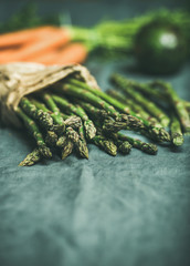 Fresh seasonal vegetables on table. Green asparagus, carrots and avocado at background over grey linen table cloth. Copy space, selective focus. Clean eating, healthy, diet, detox, vegan food concept