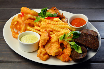 fried snacks Onion rings, chicken wings, bread with sauce on a plate
