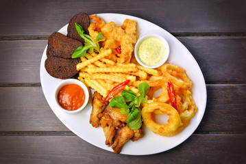 Assorted fried snacks Onion rings, chicken wings, bread with sauce top view