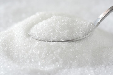 Spoon with white granulated sugar on white texture background. Unhealthy food concept.