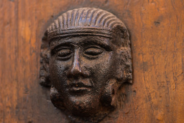 Fototapeta na wymiar brązowa kołatka w kształcie głowy starożytnego Egipcjanina na tle rudawej ściany