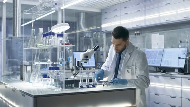 Research Scientist Looks into Microscope and Writes Down Observations. He's Conducts Experiments in Modern Laboratory.