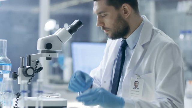 Research Scientist Looks Into Microscope and Writes Down His Observations. He's Working in a Modern Laboratory. Shot on RED EPIC-W 8K Helium Cinema Camera.