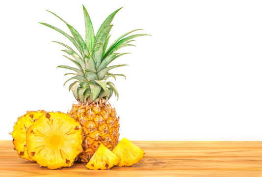 pineapple fruit with sliced pineapple fruit on wooden table with white wall background