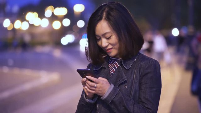 Smiling young Chinese woman typing on the smartphone and smiling at the camera
