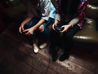Fototapeta na wymiar Two unrecognizable girls play video game with joysticks in hands. Entertainment, leisure, fun, high tension and excitement concept
