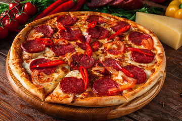 Fresh homemade pizza with tomatoes, salami, chili pepper, and cheese on wooden background. Italian restaurant menu photo.