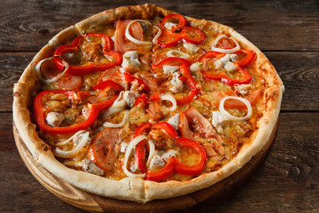 Italian cuisine, traditional fast food. Appetizing colorful fresh pizza with ham, cheese, tomato, paprika and onion served on rustic wooden table, top view.