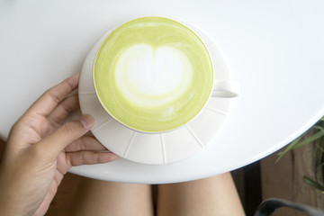 lady hands holding a cup of green matcha latte coffee art on white table background. top view.