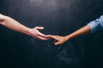 Reconnection of relationship or breakup.Two hands hold each other. Unrecognizable white guy and black woman on a dark background holding hands.