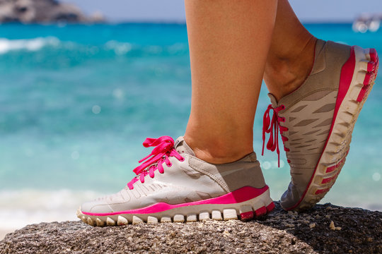 Runner woman stands on a rock near the blue sea. Red laces gray sneakers. Closeup. Photo knee © dadoodas