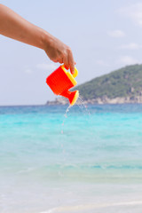 Female hand pours water from a children's plastic watering can. Andaman sea, Similan Islands