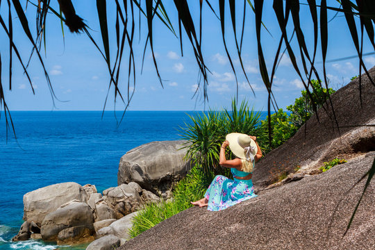 Girl in a blue dress is sitting on stone and looking into the distance of the horizon