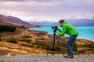 Travel photographer taking nature landscape pictures in New Zealand at sunset. Man shooting at Peter's lookout, famous tourist attraction at Pukaki Lake. - obrazy, fototapety, plakaty