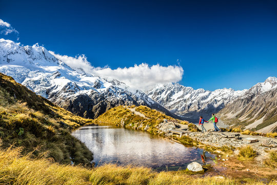 Hiking travel nature hikers in New Zealand. Couple people walking on Sealy Tarns hike trail route with Mount Cook landscape, famous tourist attraction.